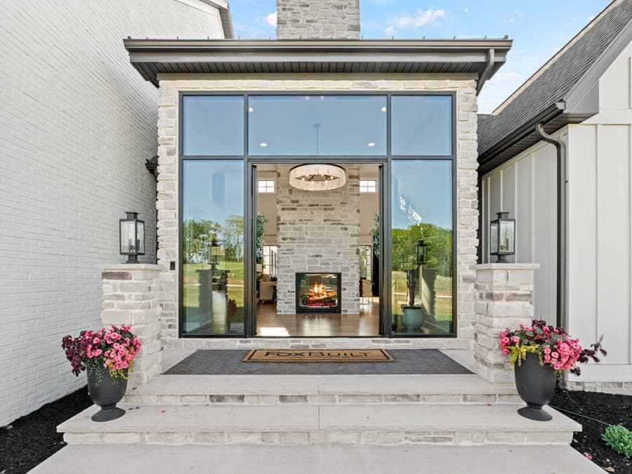 A glass entry framed in stone, with a lit two sided fireplace visible through the windows
