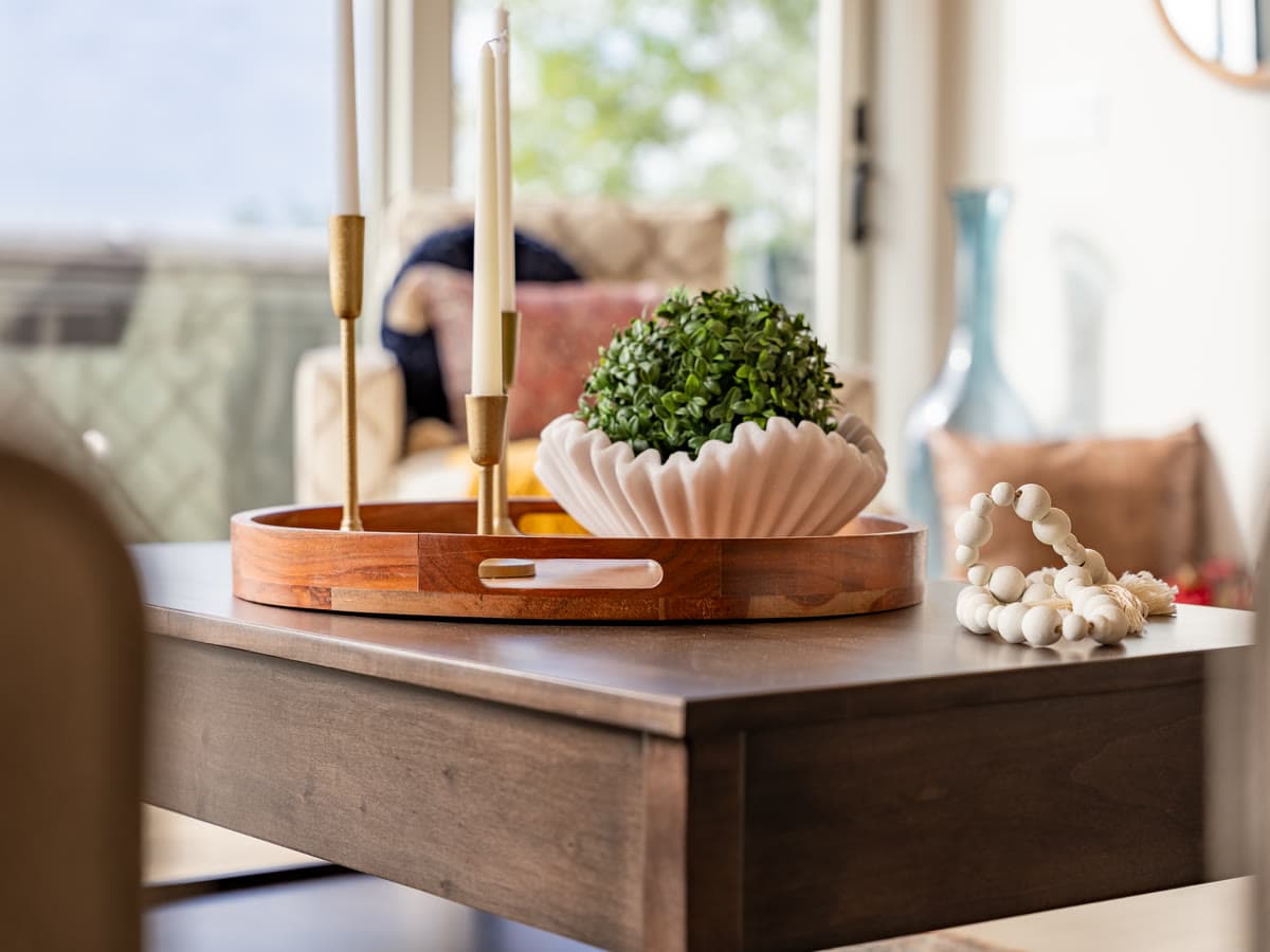 A styled table with brass candlesticks, a wooden tray, and a fluted white bowl of greenery