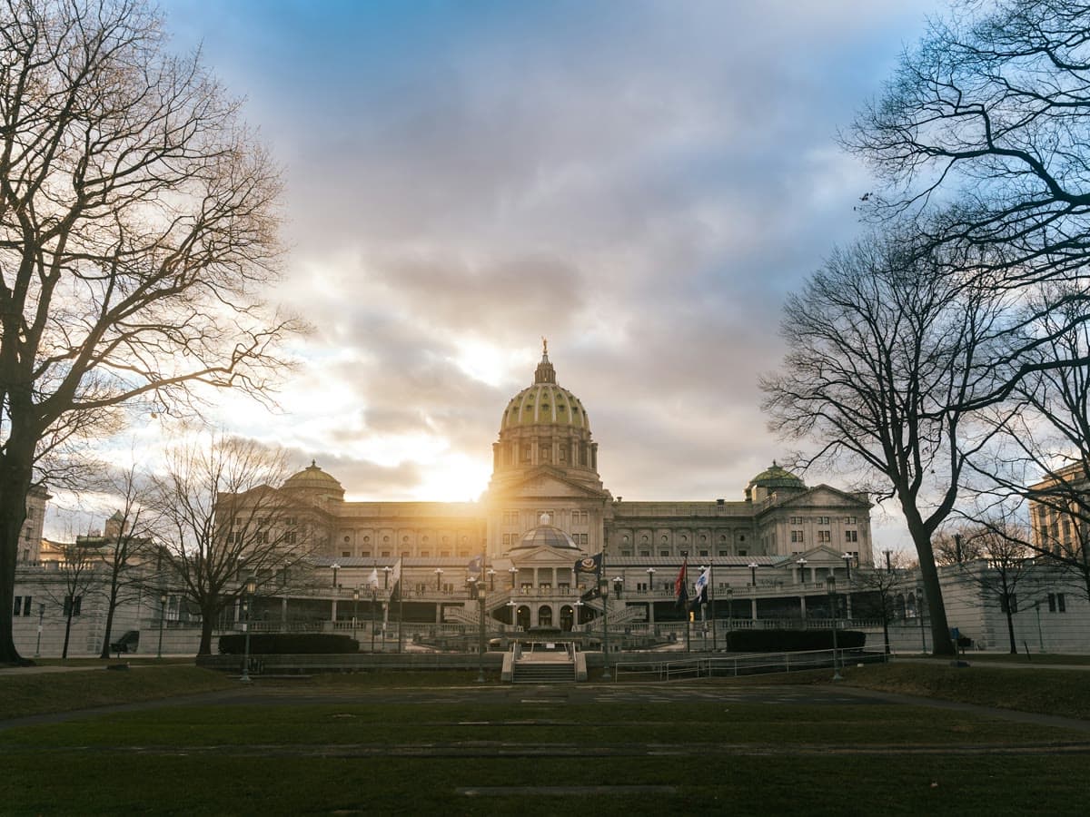 The Pennsylvania State Capitol at sunset, framed by bare trees