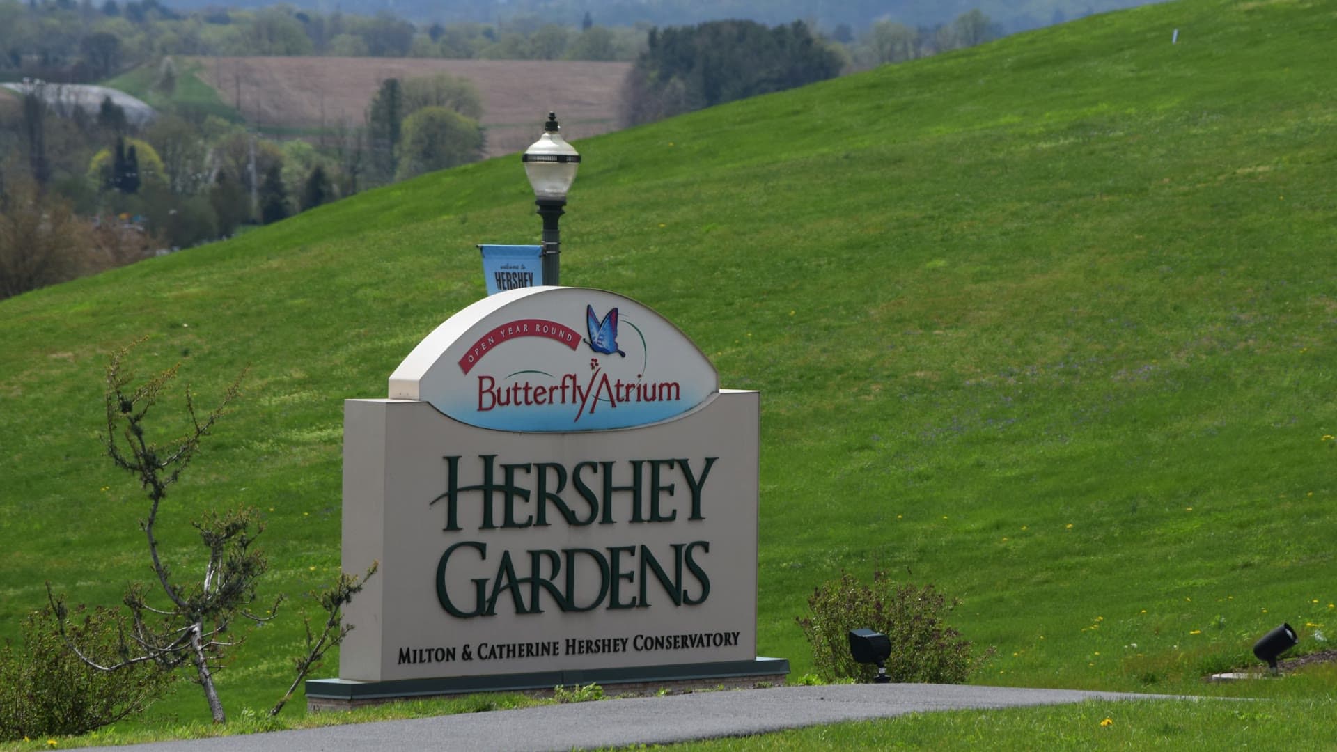 The Hershey Gardens sign on a grassy hill, with farmland beyond