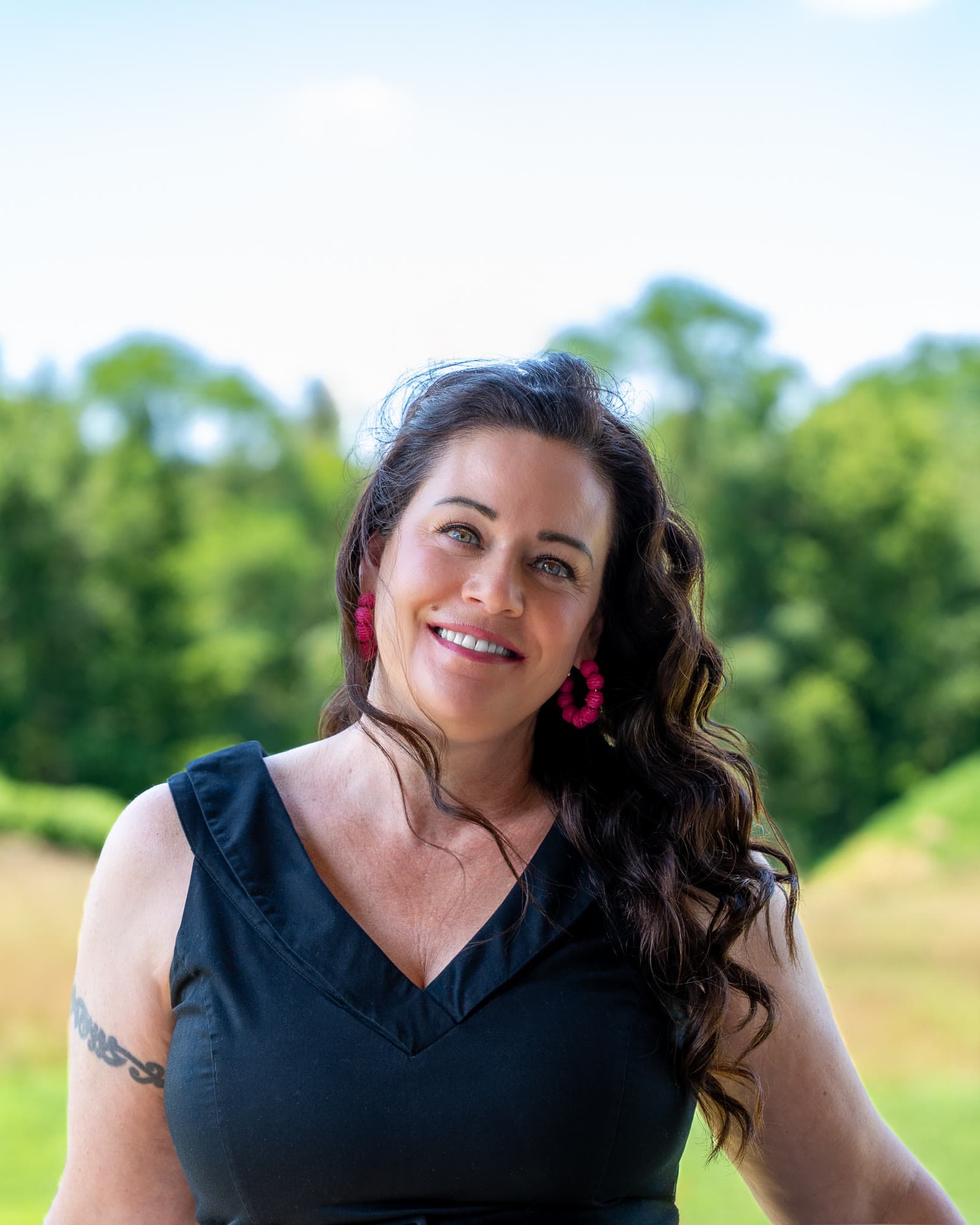 Shannon Clayton smiling outdoors, with a meadow and a line of trees behind her