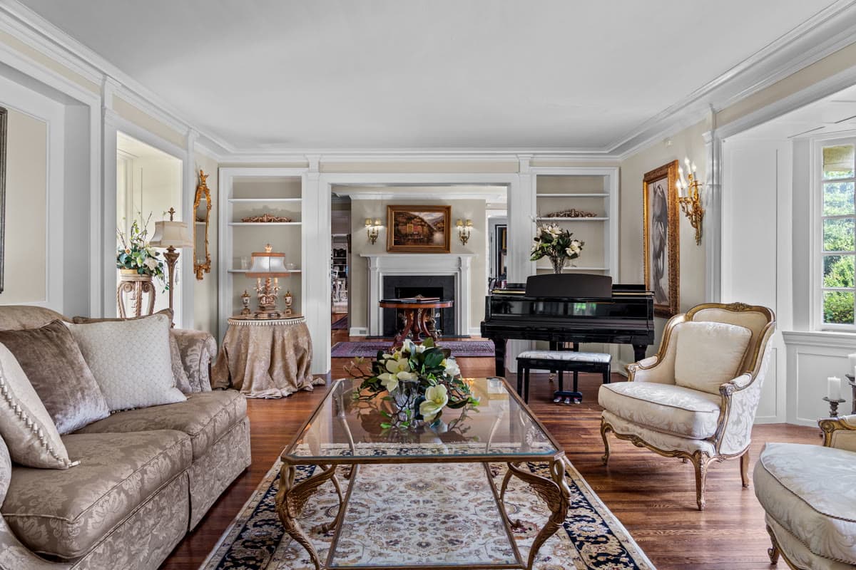 A sitting room with a grand piano, a fireplace, and upholstered armchairs