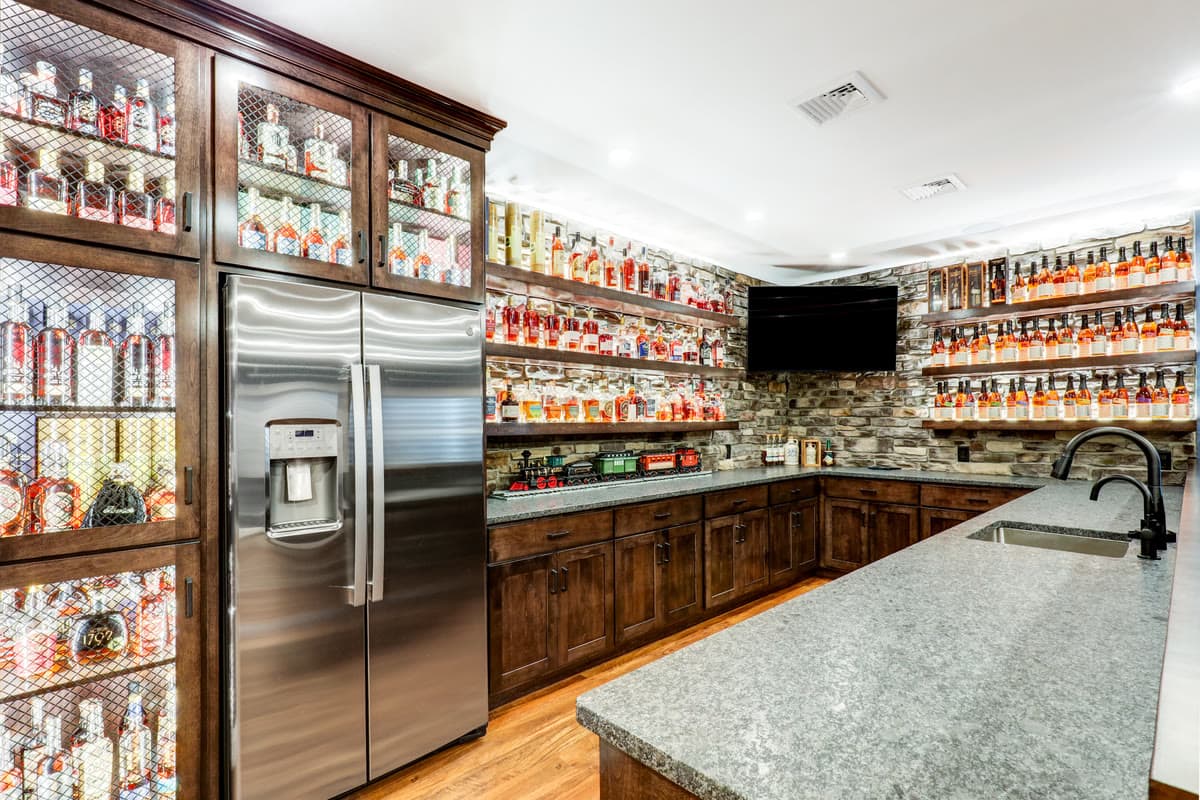 A lower level bar with glass fronted display cabinets, stone walls, and a granite counter