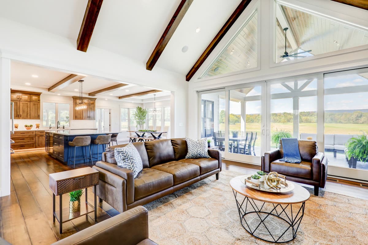 A great room under exposed timber trusses, with leather sofas and a wall of windows onto open fields