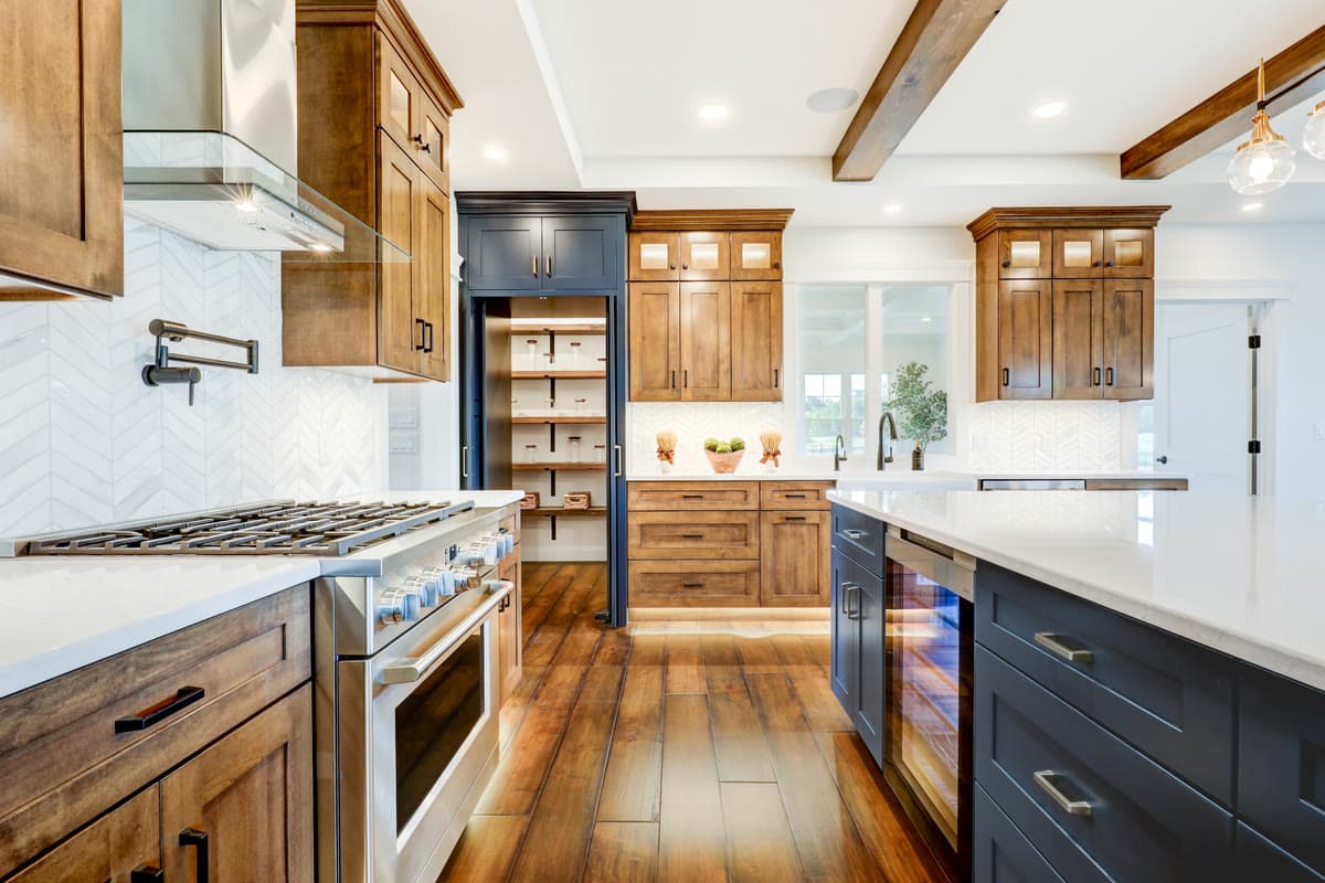 A gas range under a wood hood, with a pot filler, white tile, and a navy pantry door