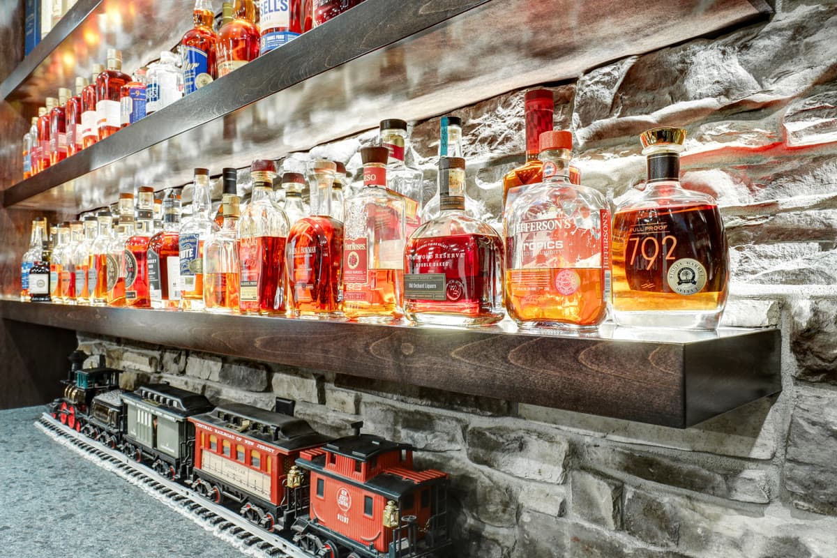 Lit floating shelves of bottles over a stone wall, with a model train running beneath