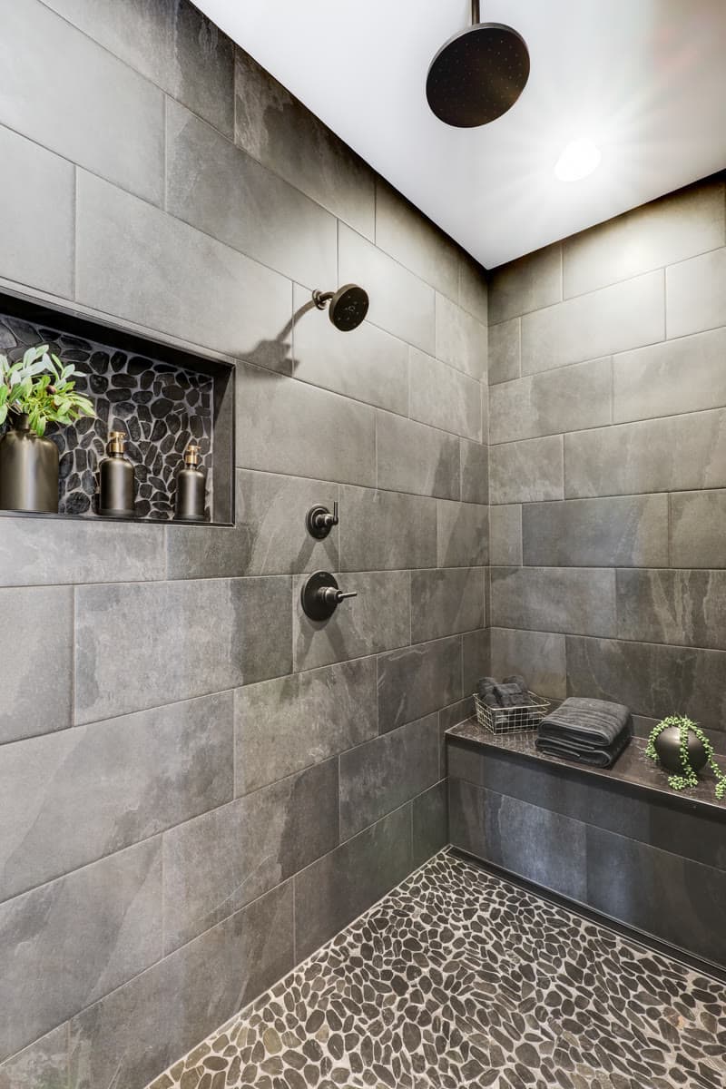 A walk in shower in grey tile with a pebble floor and a recessed niche