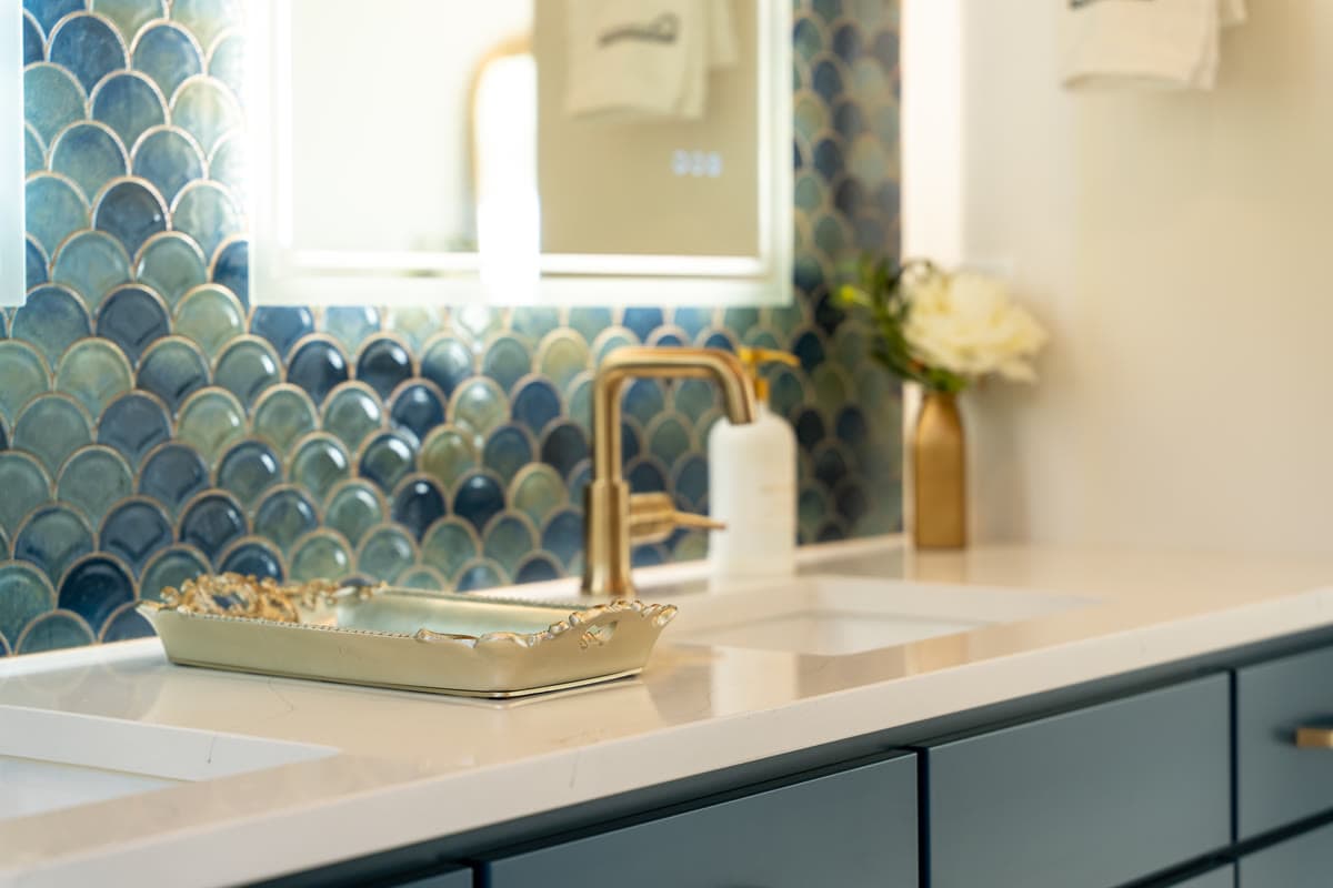 A bath vanity with a brass faucet against blue fish scale tile