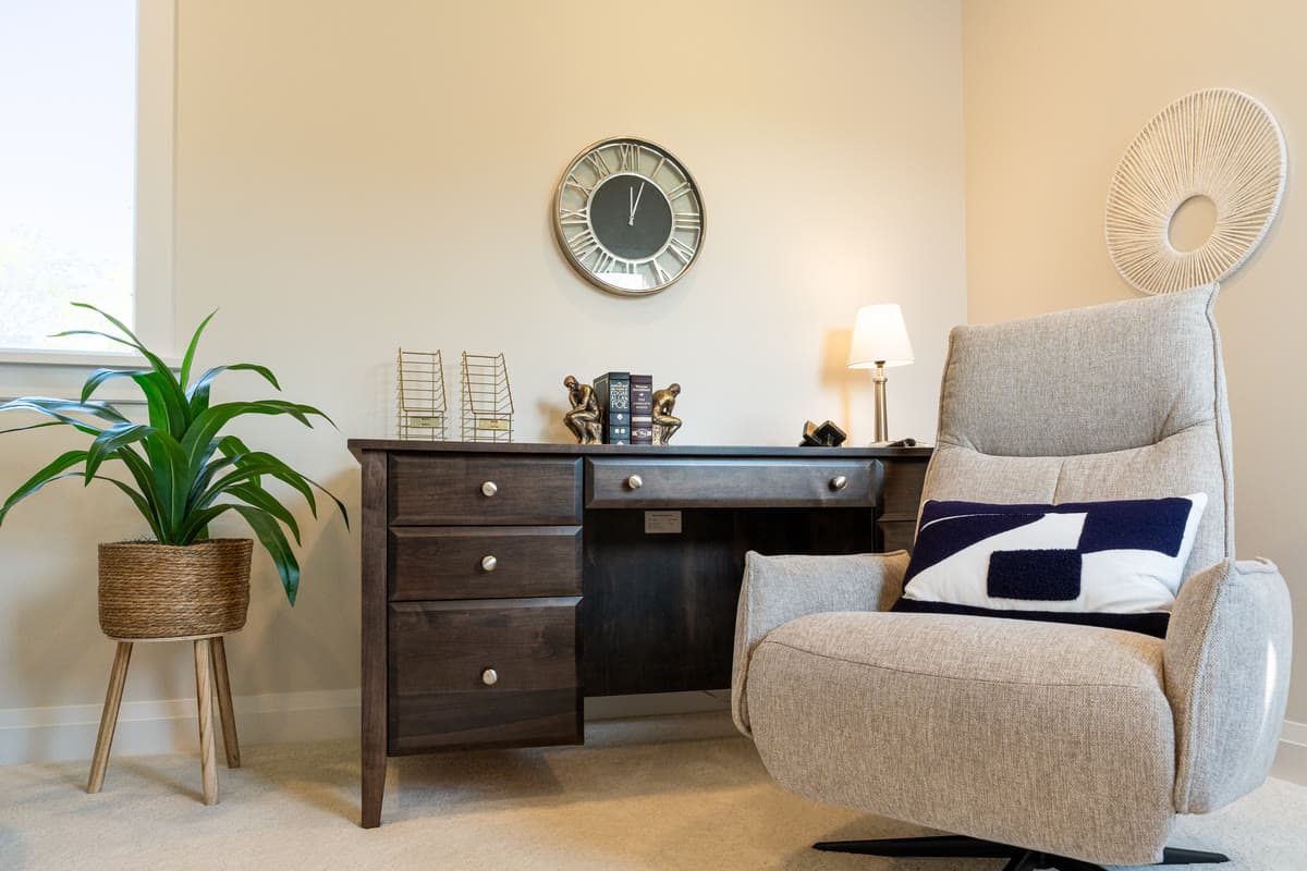 A study corner with a dark wood desk, a wall clock, and a grey swivel armchair