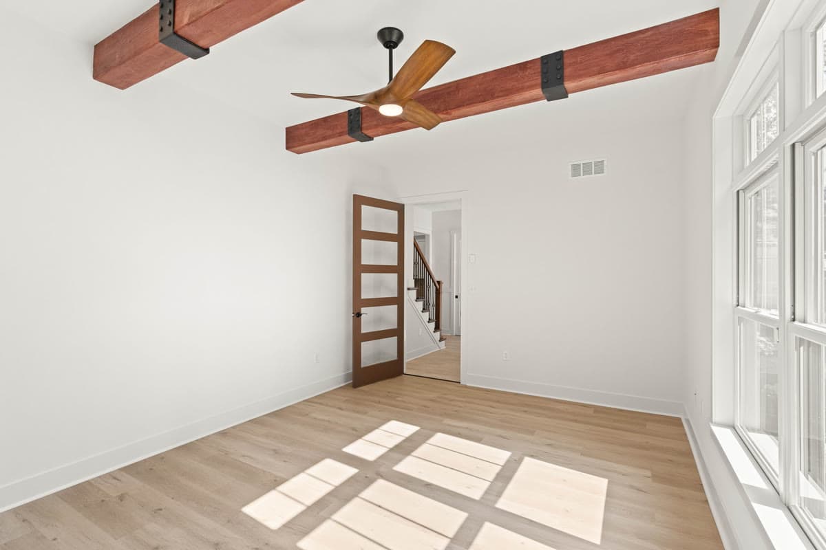 A room with a beamed ceiling, a ceiling fan, and a wood door with glass panels