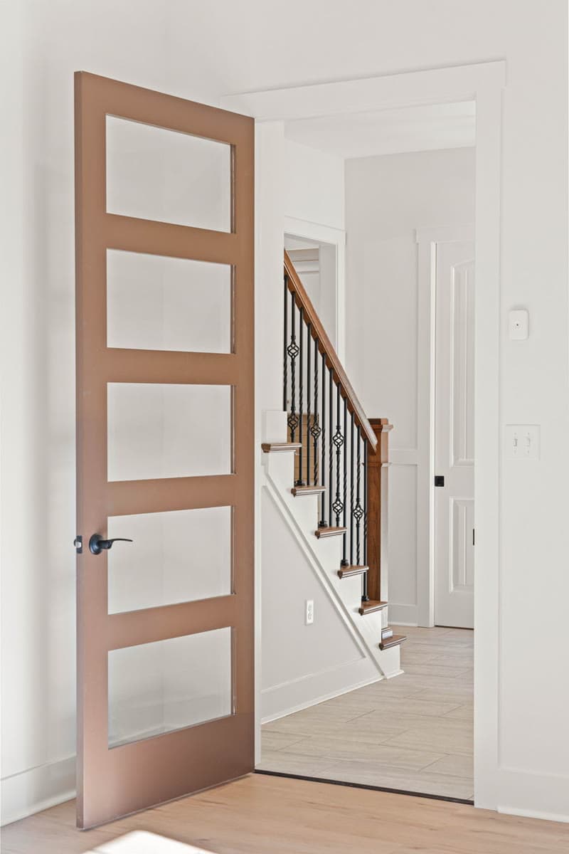 A wood interior door with frosted glass panels, open onto a staircase