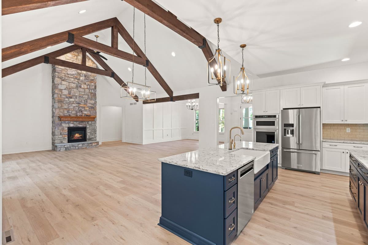An open kitchen and great room under timber trusses, with a stone fireplace