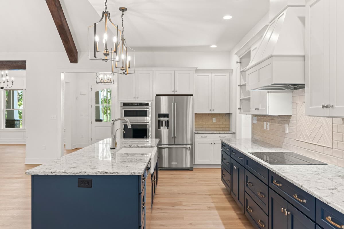 A kitchen with a navy island, white cabinetry, and brass pendant lights under a timber beam