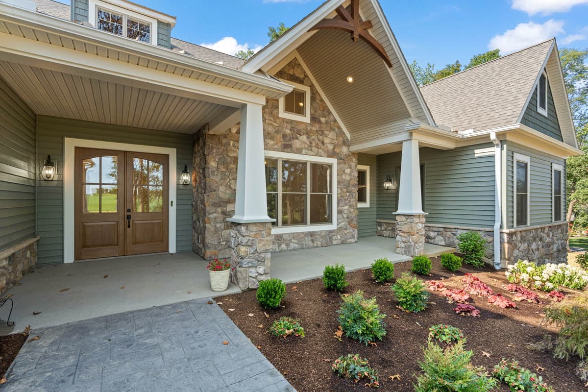 A covered entry with stone columns, a timber gable, and double wood doors