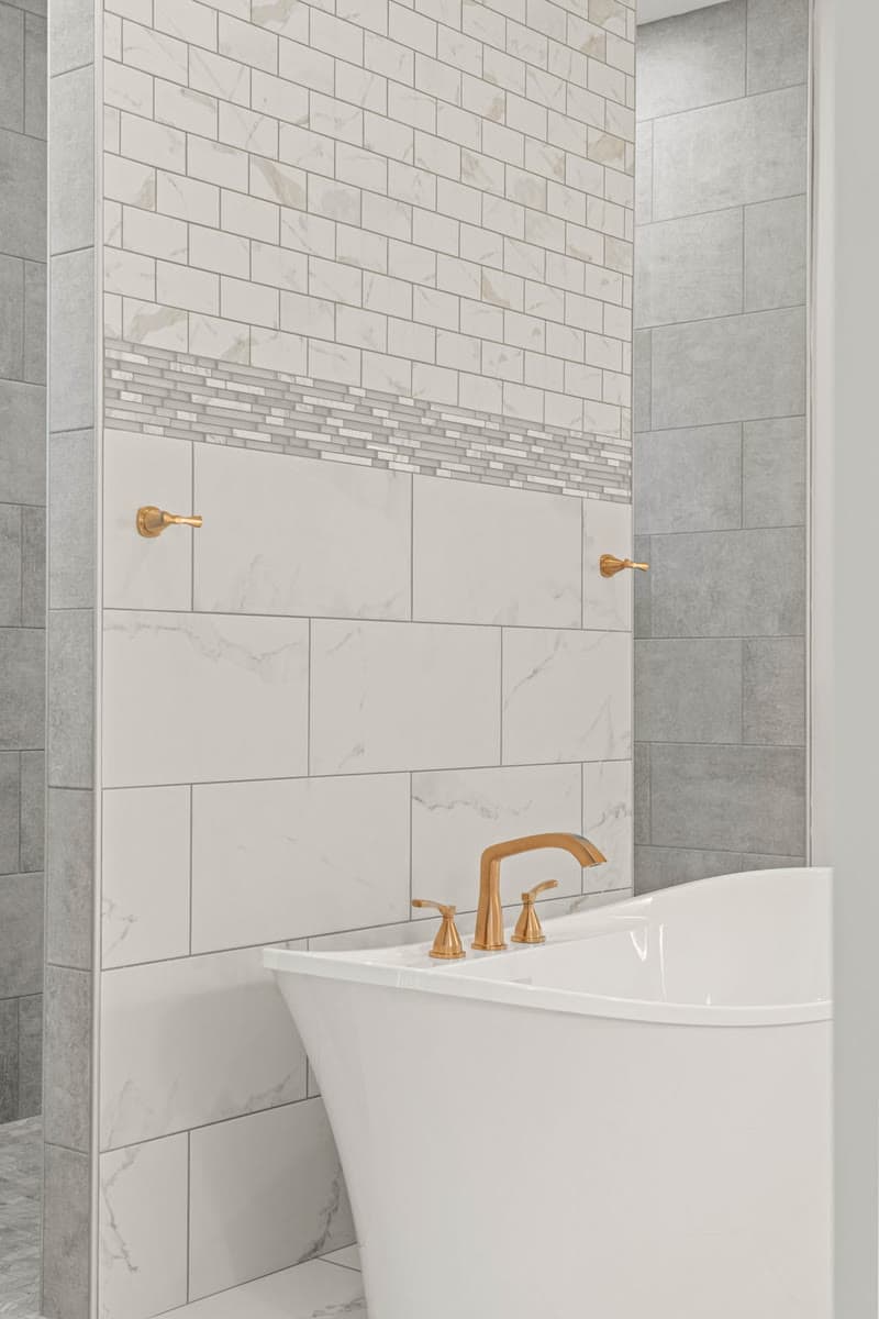 A freestanding tub with a brass filler against white marble tile